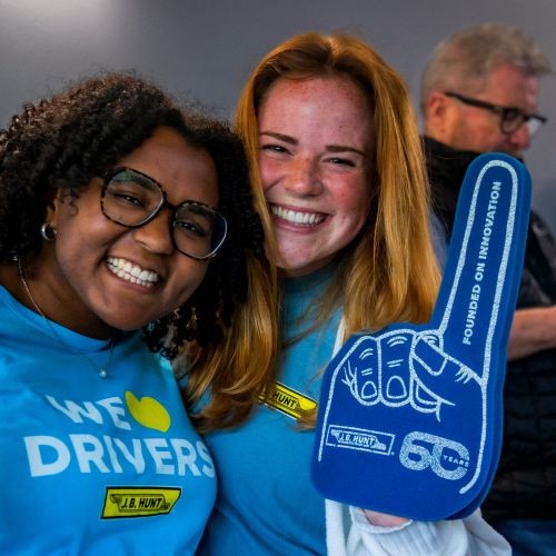 Two J.B. Hunt employees smiling and holding up a J.B. Hunt foam finger that reads,' Founded on Innovation."