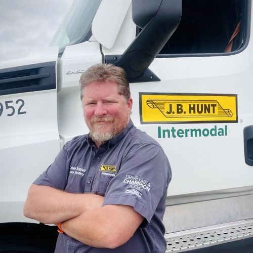 J.B. Hunt driver is standing in front of a J.B. Hunt Intermodal truck with his arms confidently crossed.