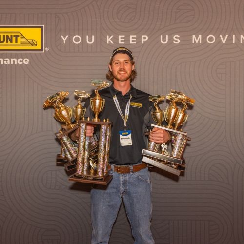 J.B. Hunt technician smiles while holding several trophies in his hands.