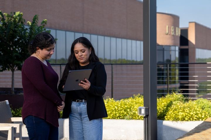 Two employees standing outside a J.B. Hunt office building reviewing information on a tablet, with the company logo visible on the building.