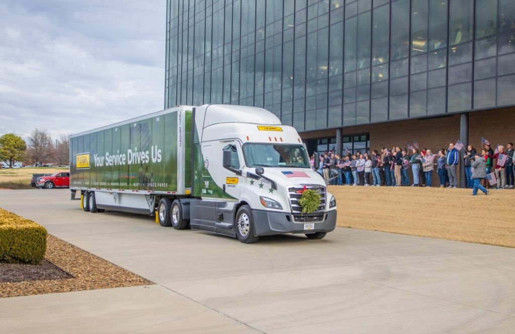 J.B. Hunt military-wrapped semi-truck with the words 'Your Service Drives Us' parked in front of a building with people cheering.