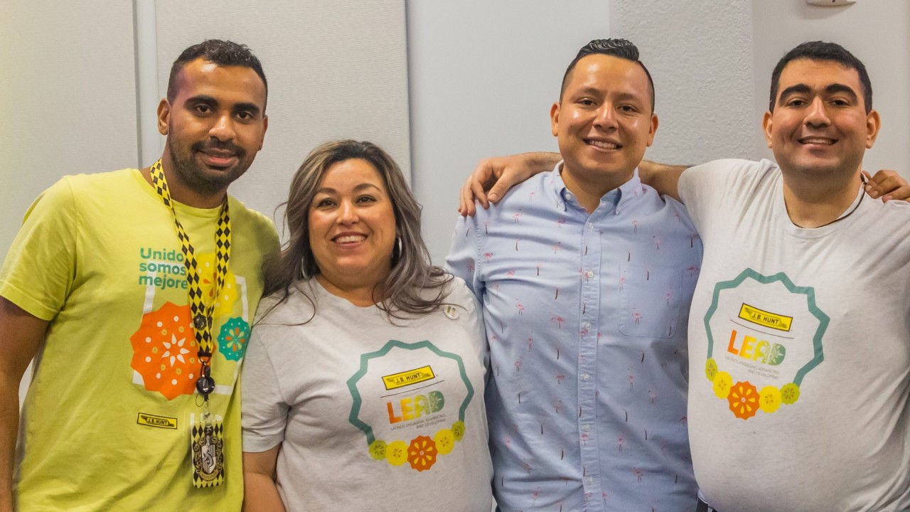 Four employees wearing LEAD shirts stand with their arms around one another.