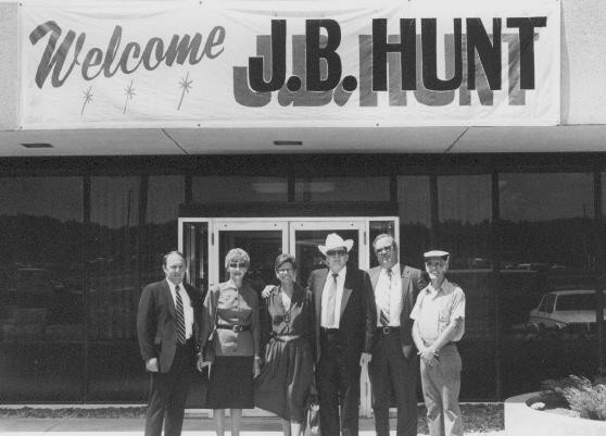 J.B. and Johnelle Hunt with a group of others posing for a picture in front of a banner reading "Welcome, J.B. Hunt".