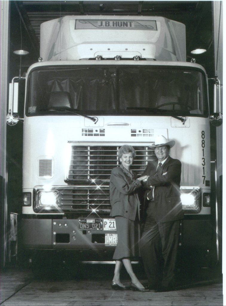 Mr. and Mrs. Hunt holding hands in front of a white J.B. Hunt semi truck