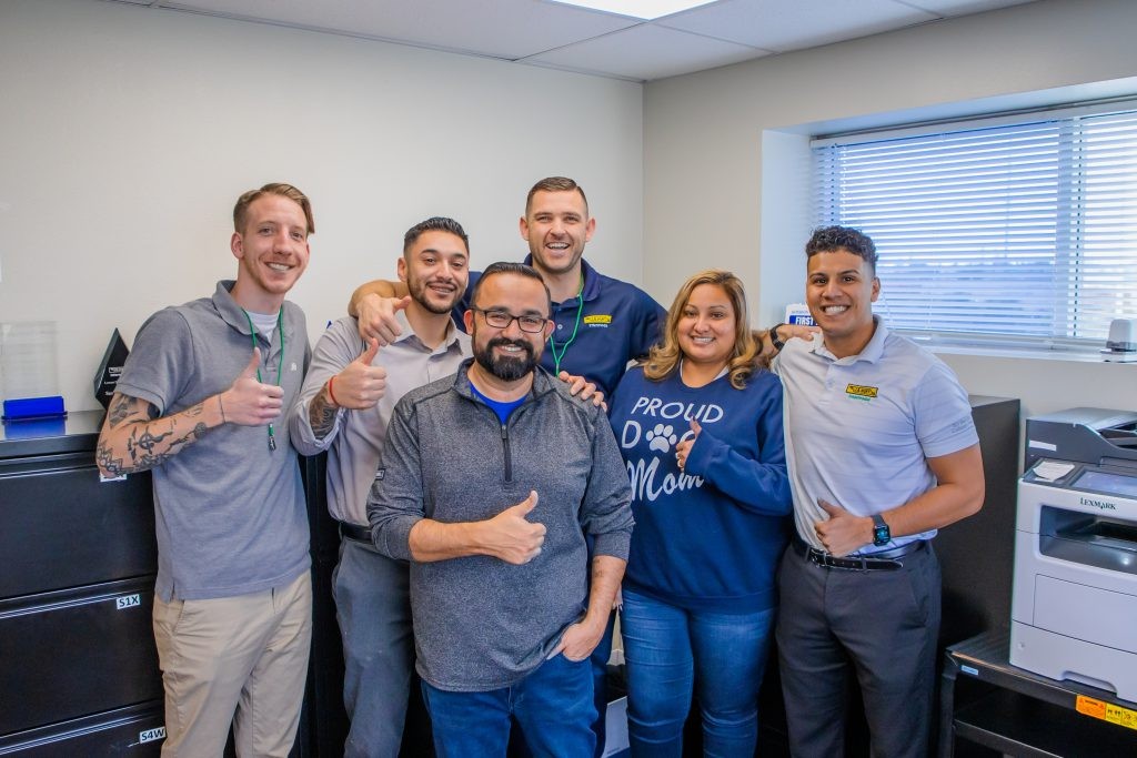 A group of J.B. Hunt employees smiling and giving a thumbs up in an office.