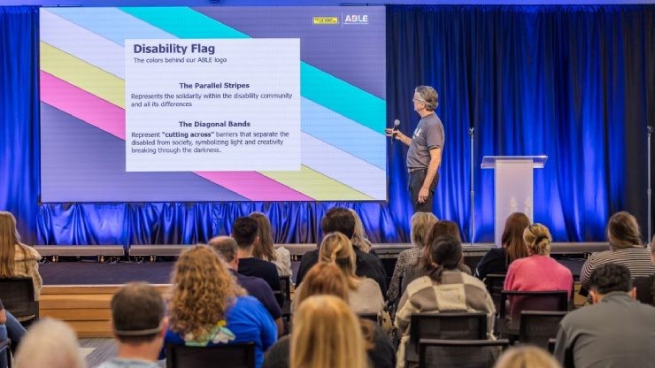 J.B. Hunt employee presenting the meaning behind the Disability Flag and ABLE logo during the ABLE ERG launch event, with an audience seated in front.