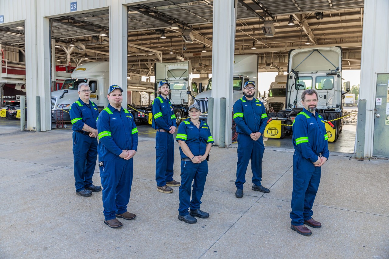 A group of maintenance techs standing in front of maintenance shop.