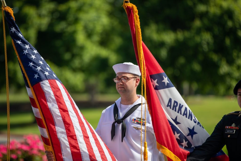 J.B. Hunt military employee holds American flag next to the Arkansas state flag.