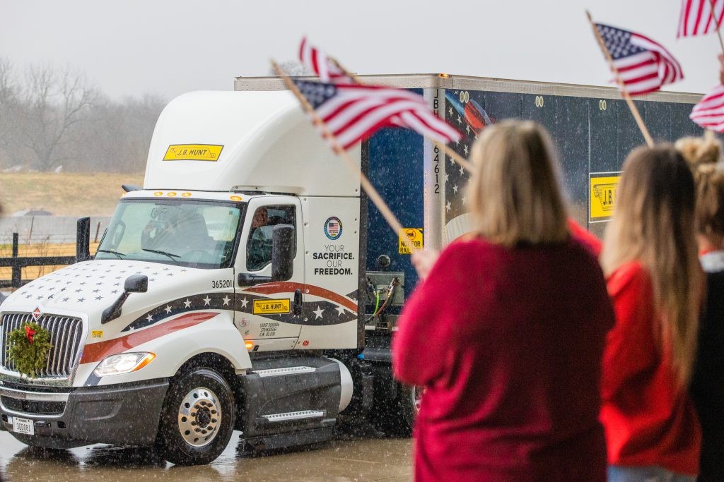 J.B. Hunt employees wave American flags in front of a J.B. Hunt tractor trailer during the Wreaths Across America ceremony.