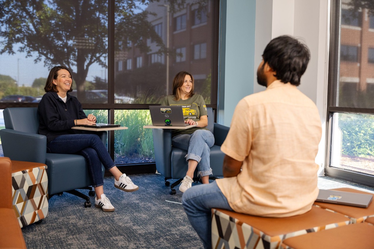 Three employees conversing at an indoor commons area.