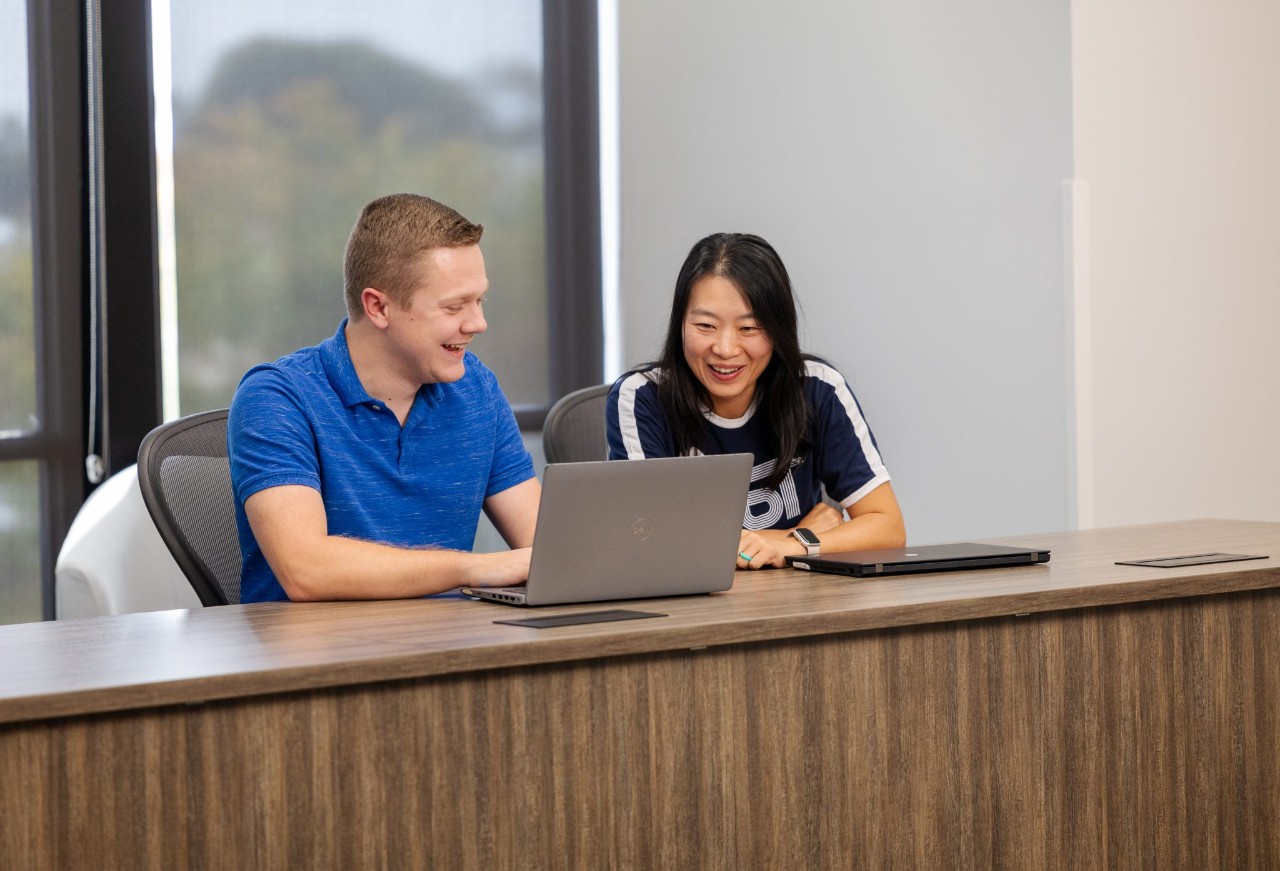 Two employees collaborating on a laptop in a meeting room.