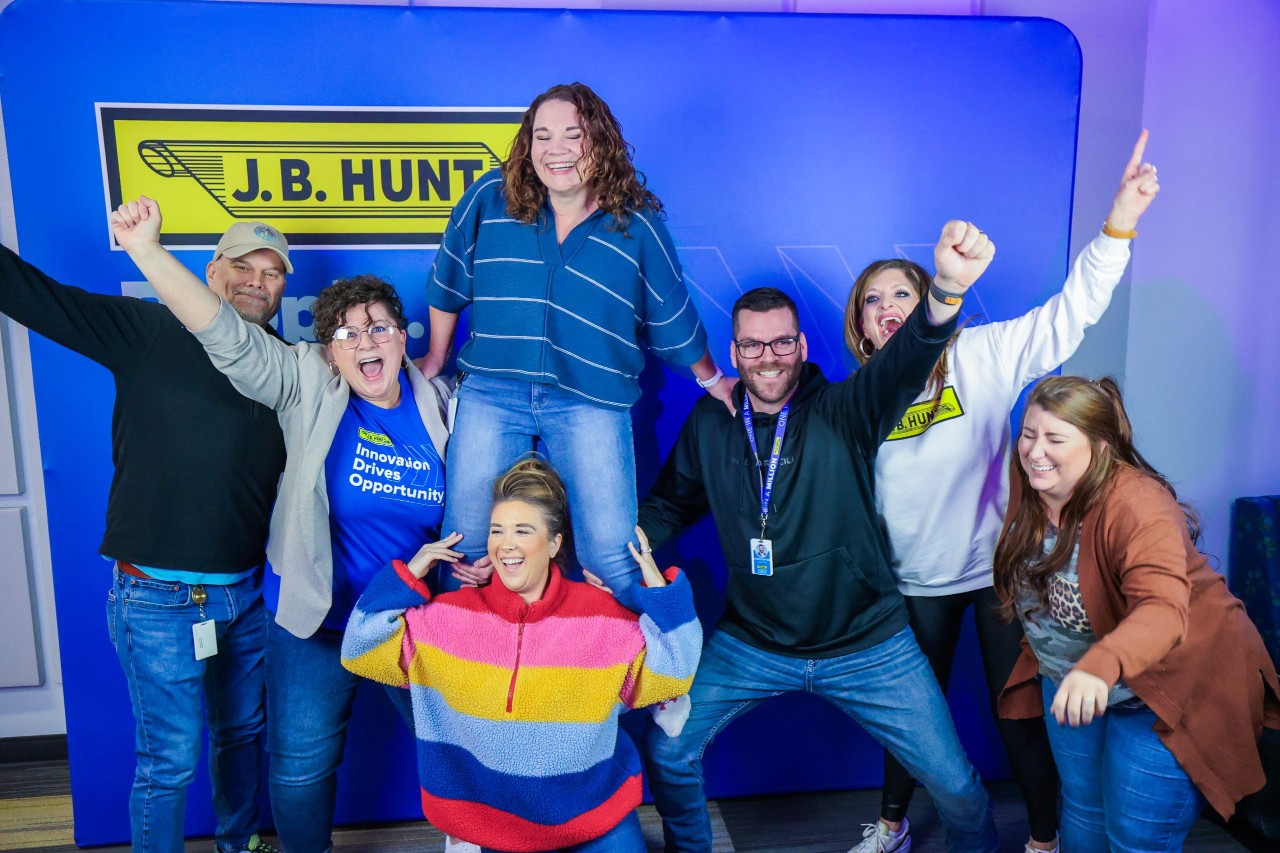 group photo of J.B. Hunt employees cheering in front of a J.B. Hunt backdrop.