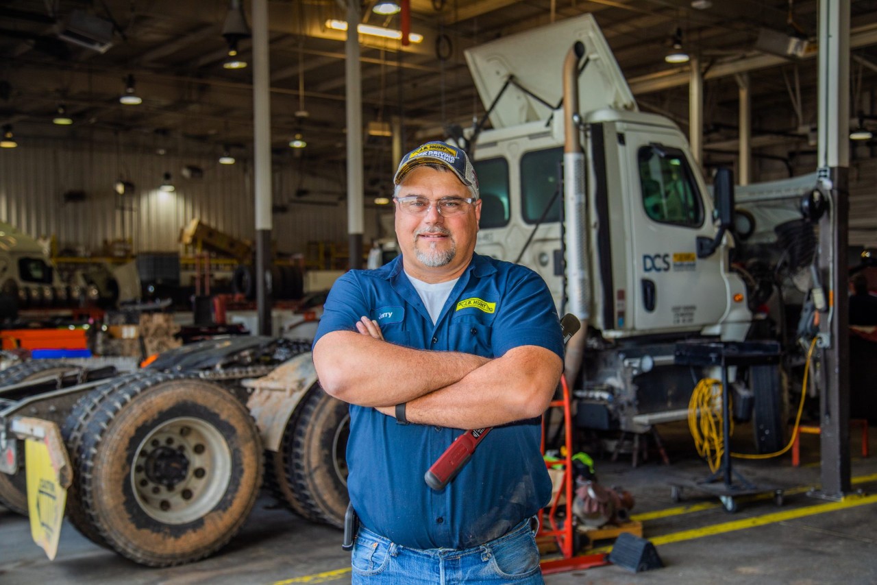 A maintenance technician posing for a picture with arms crossed inside a maintenance shop.