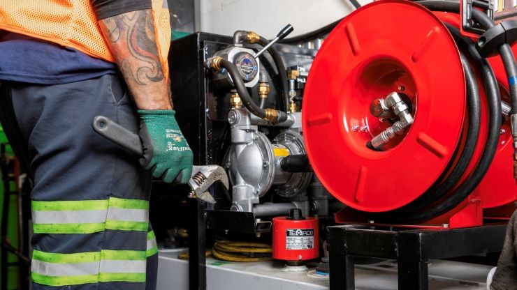 Close-up of a diesel technician using tools to service equipment with a red hose reel in a workshop setting