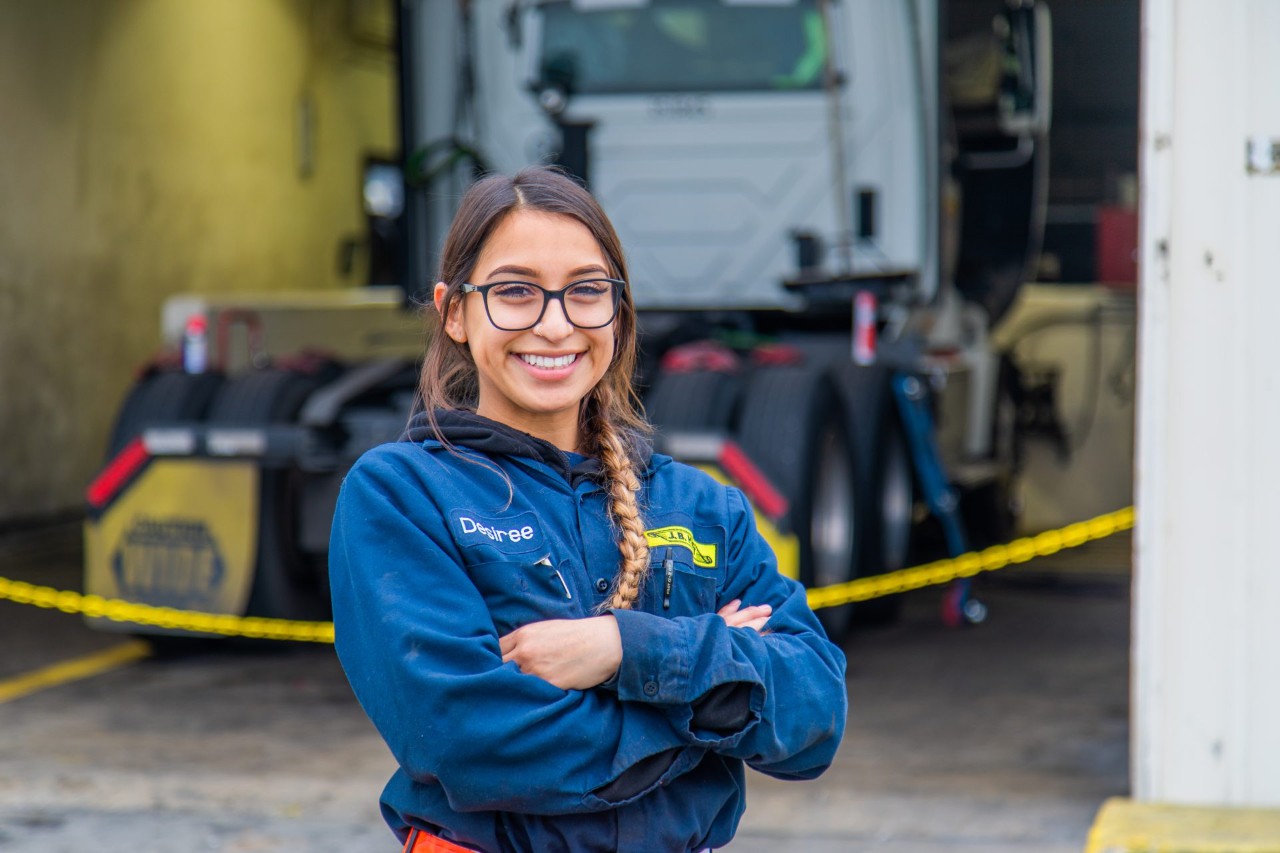 Desiree standing in front of maintenance bay with arms crossed.