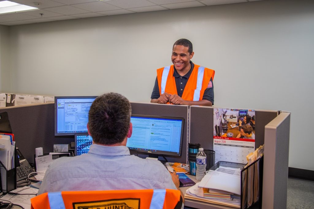 A J.B. Hunt operations employee in a high visibility vest smiling by a desk.