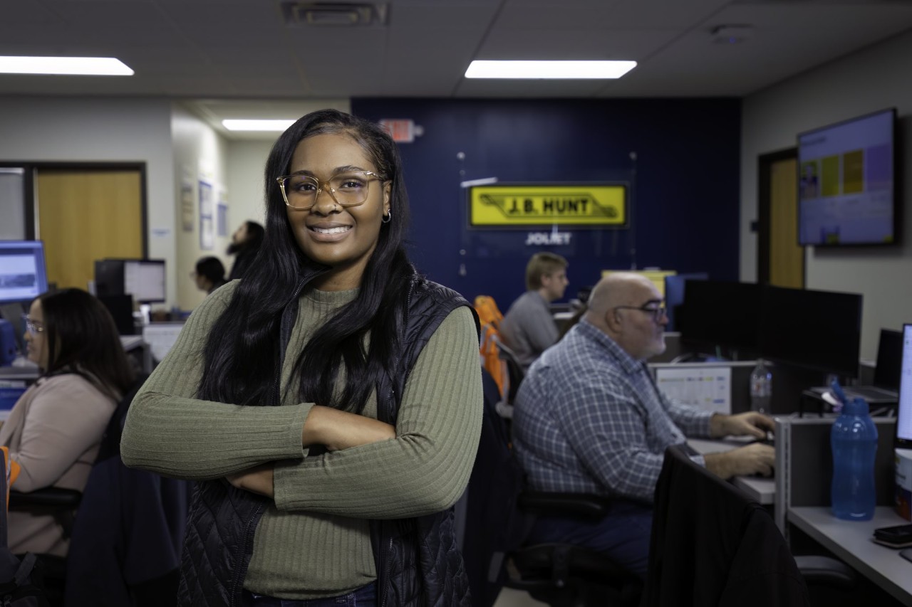 Woman standing inside office building with arms crossed and smiling.