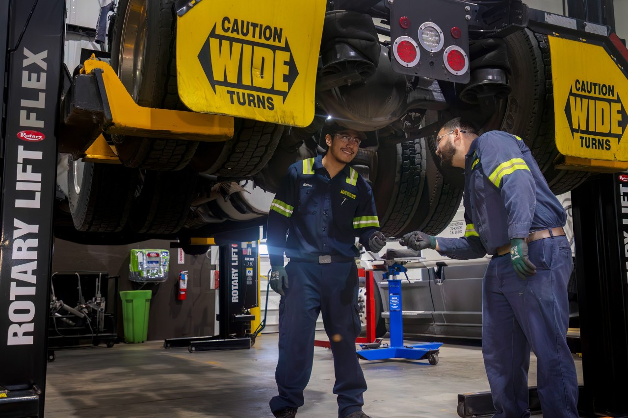 Two J.B. Hunt maintenance technicians working underneath a lifted truck