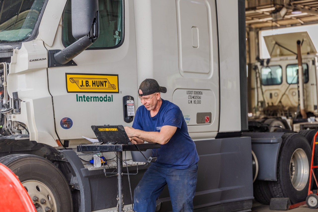 A J.B. Hunt maintenance technician working on a laptop next to a J.B. Hunt truck