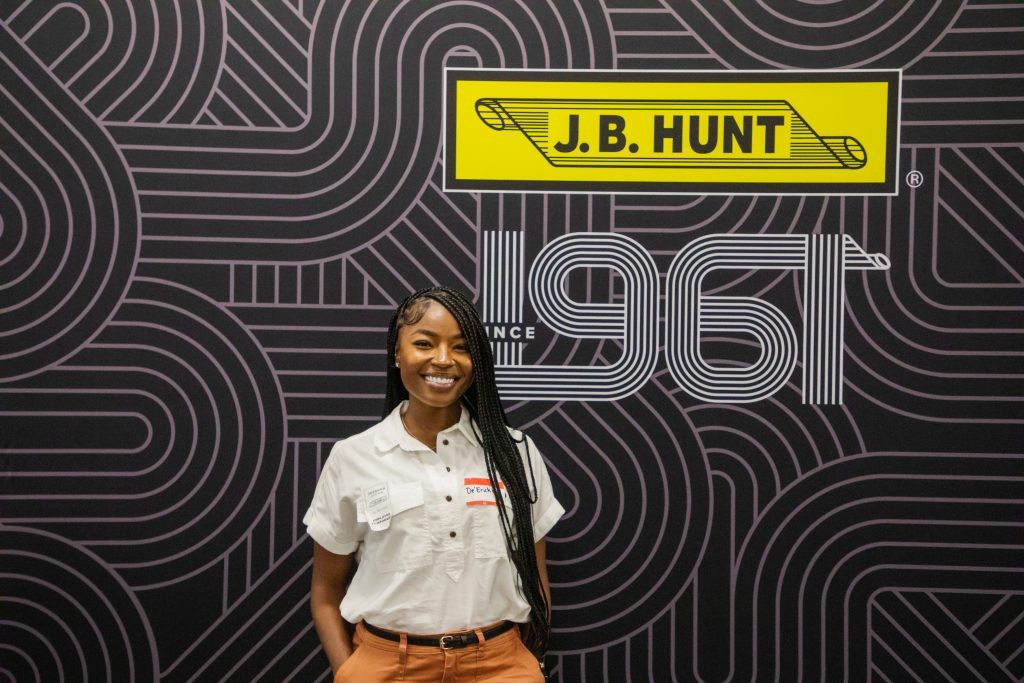 A J.B. Hunt intern standing in front of the yellow and black J.B. Hunt scroll logo.