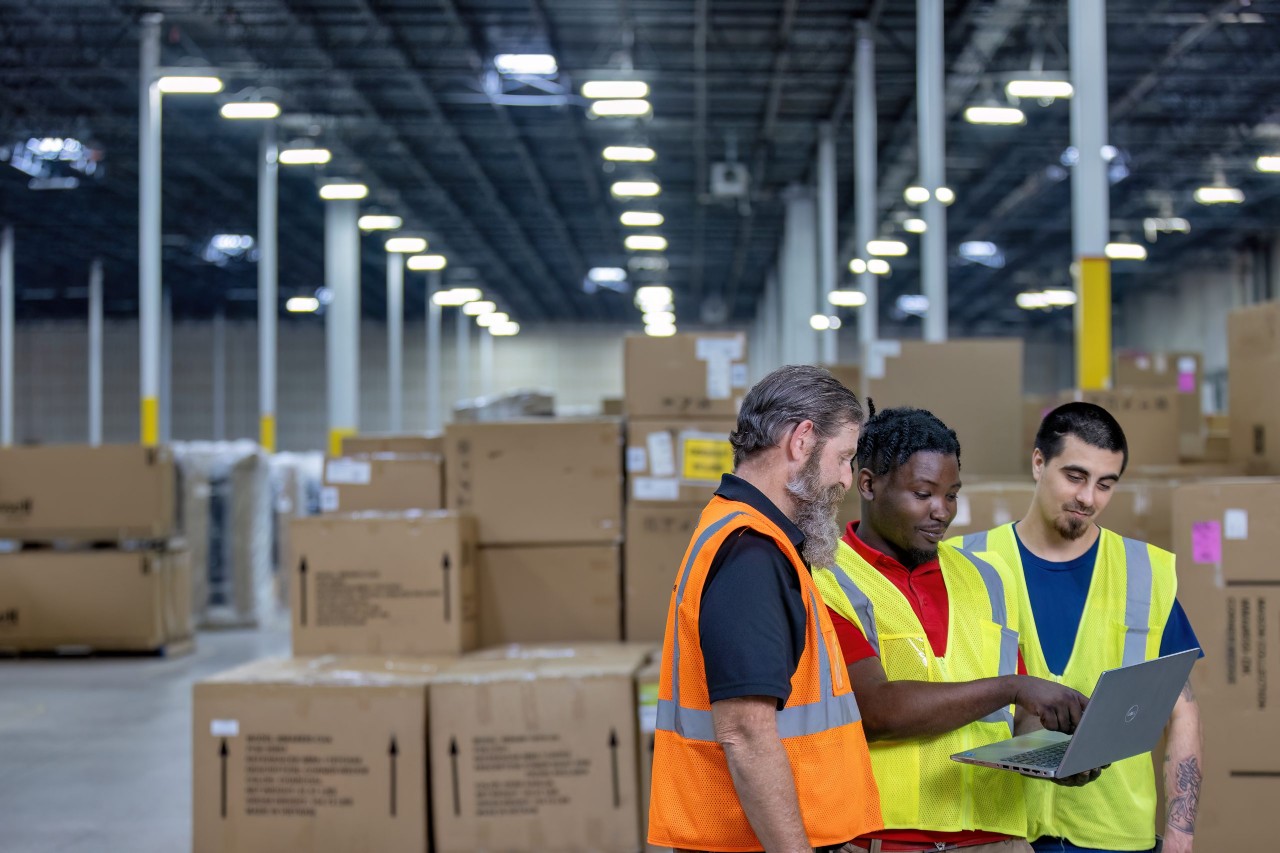 Three warehouse employees looking at a laptop.