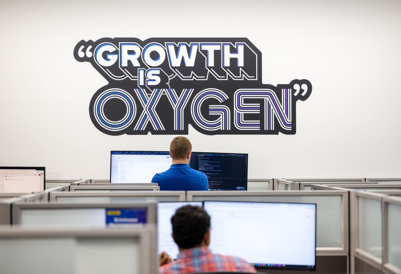 A person working at a standing desk in front of a wall decal that reads, "Growth is oxygen".
