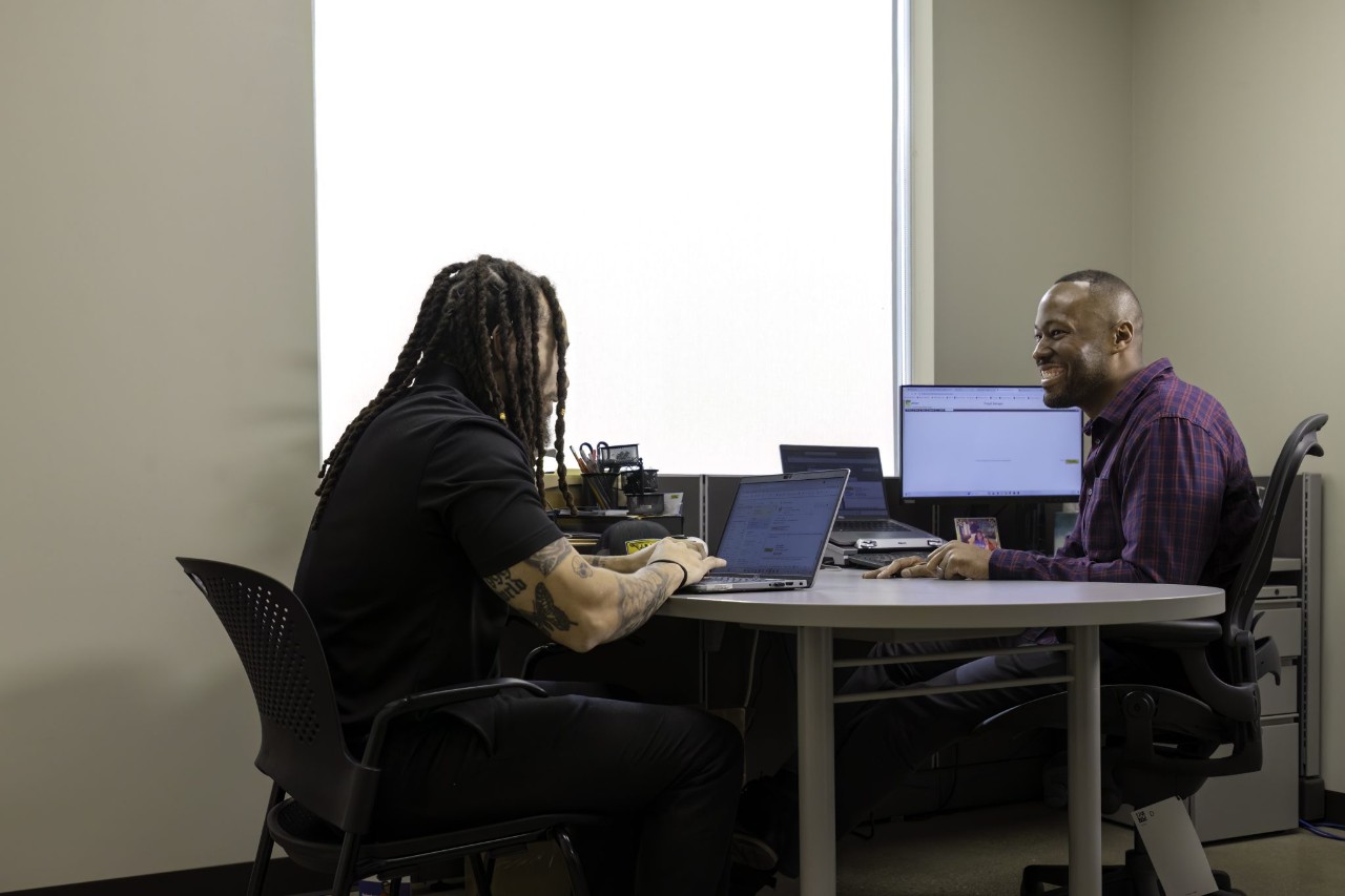 Two office employees conversing at a desk.