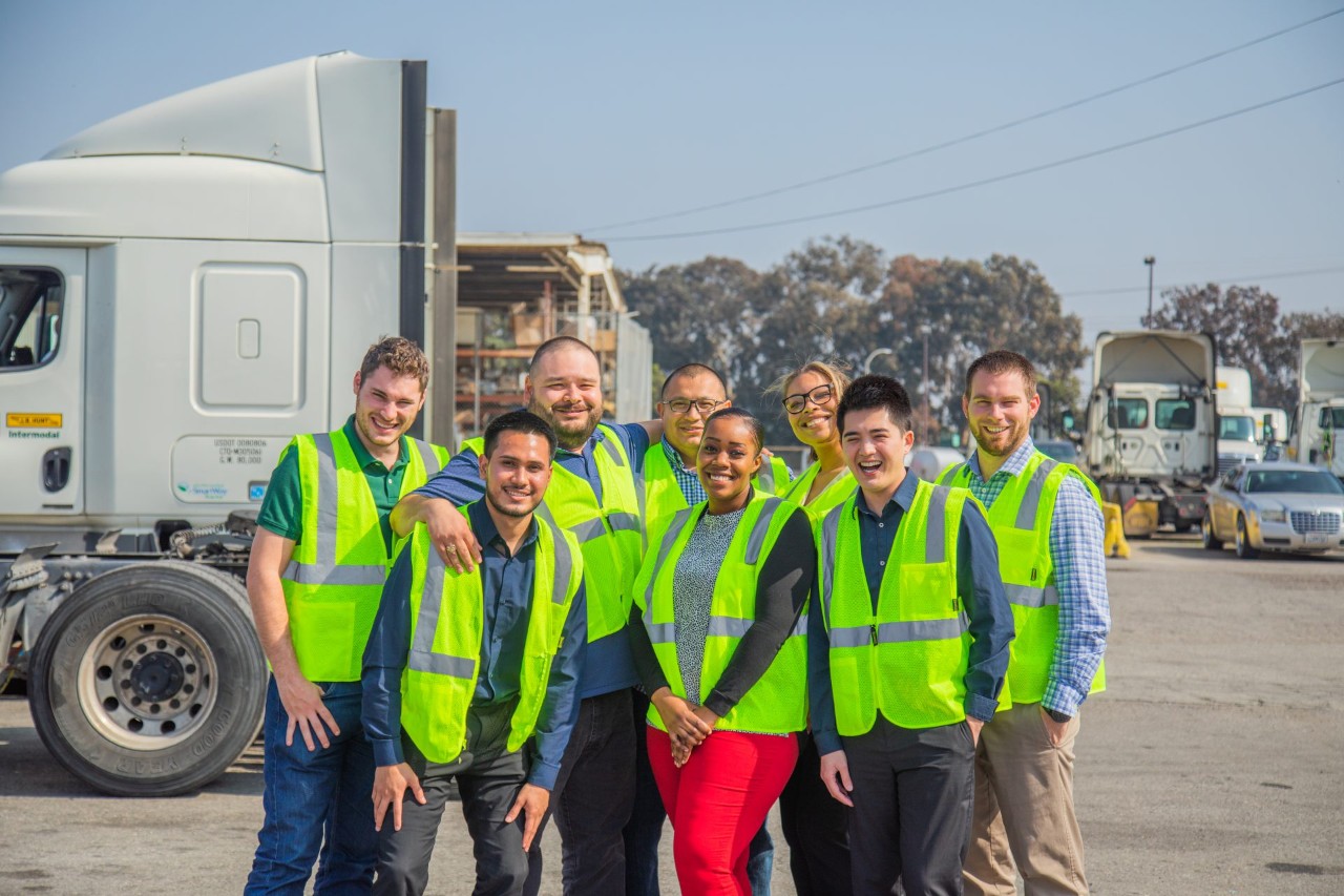 J.B. Hunt employees in high visibility vest posing for a picture in a parking lot.