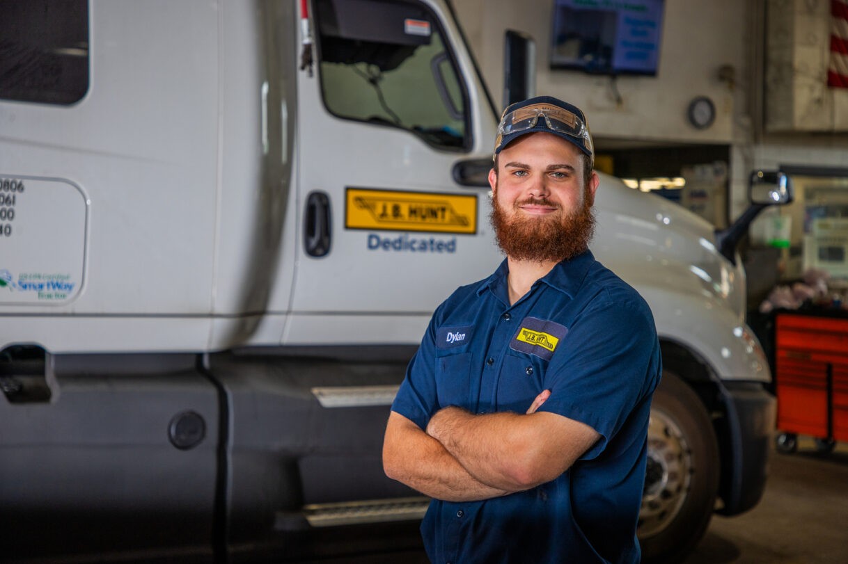 Dylan, J.B. Hunt maintenance technician, standing in front of J.B. Hunt truck in Dallas, TX shop.