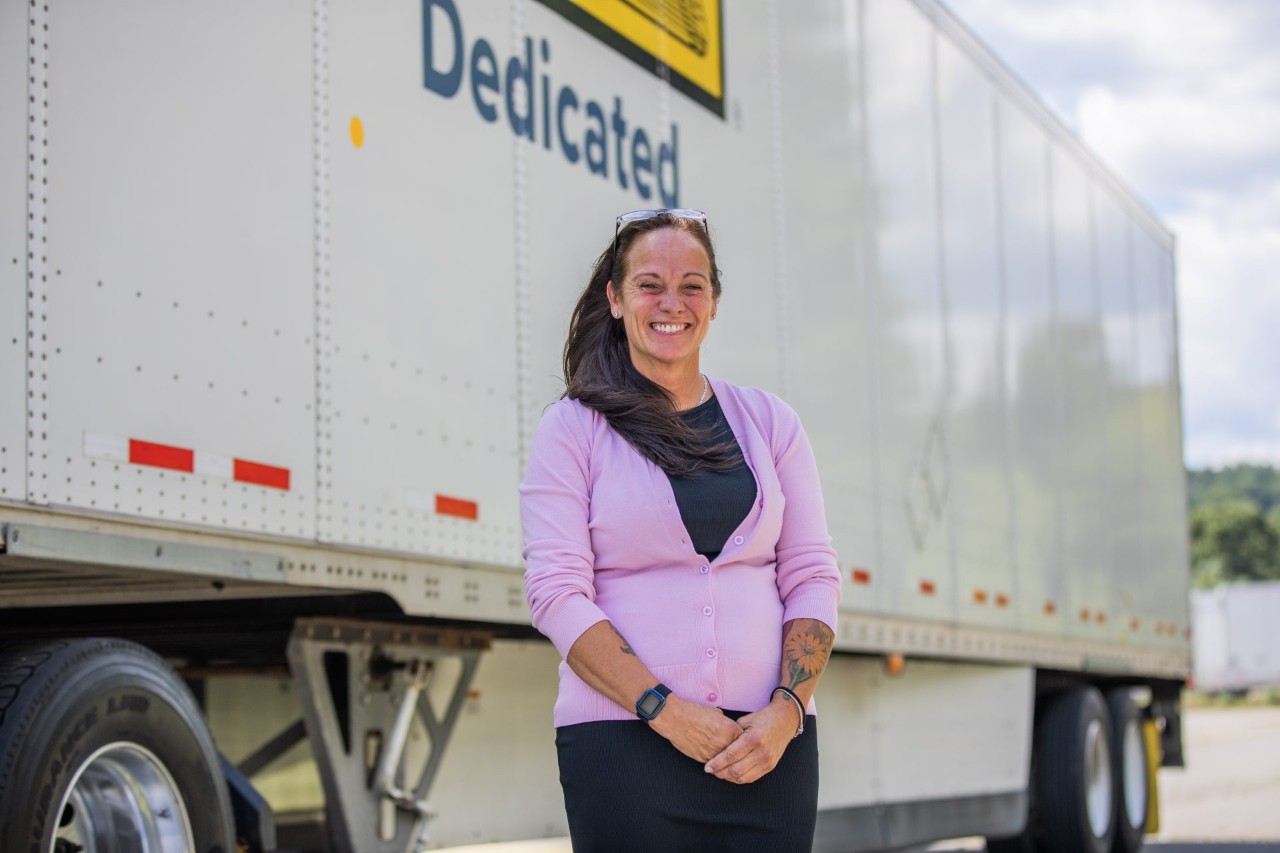 J.B. Hunt employee, Jan, standing in front of a Dedicated trailer while smiling at the camera.