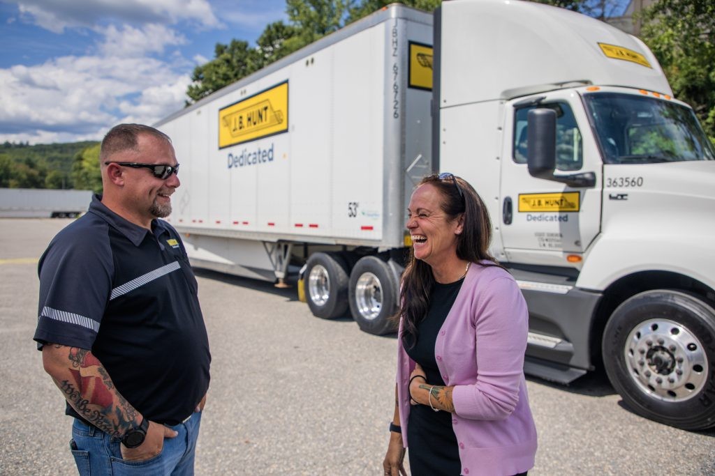 Two J.B. Hunt employees laughing in front of a white J.B. Hunt tractor trailer.