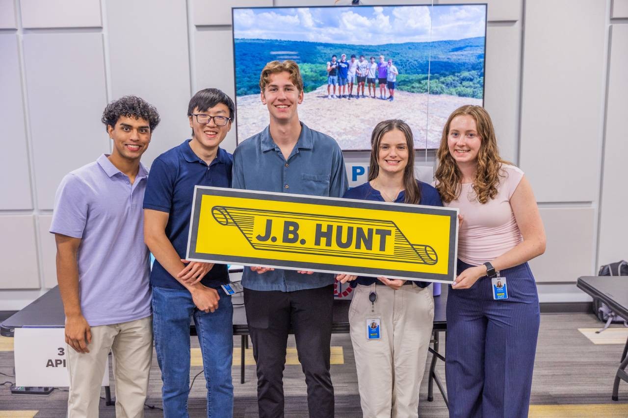 A group of interns holding a J.B. Hunt yellow scroll logo at an intern event.