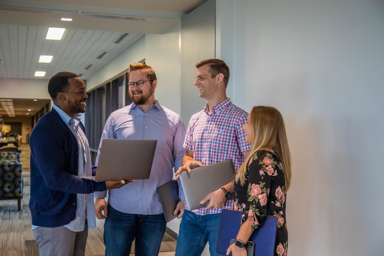 4 corporate office employees conversing in a hallway.