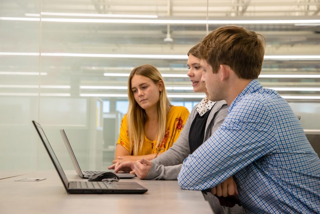 Three J.B. Hunt employees look at two laptops together in a conference room