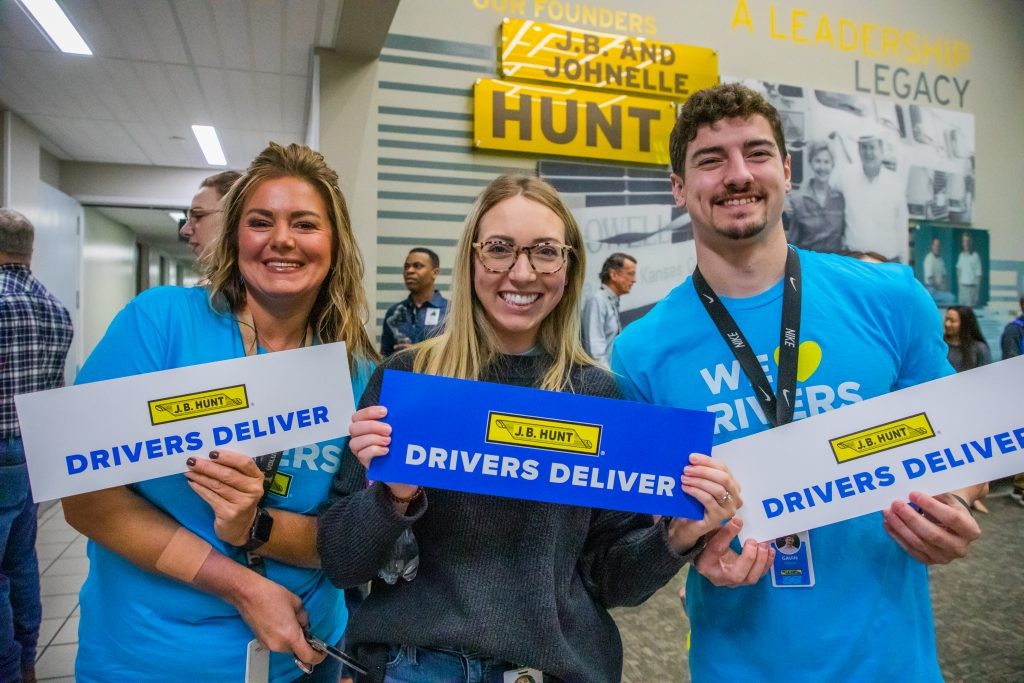 Three J.B. Hunt employees holding signs that say 'drivers deliver'