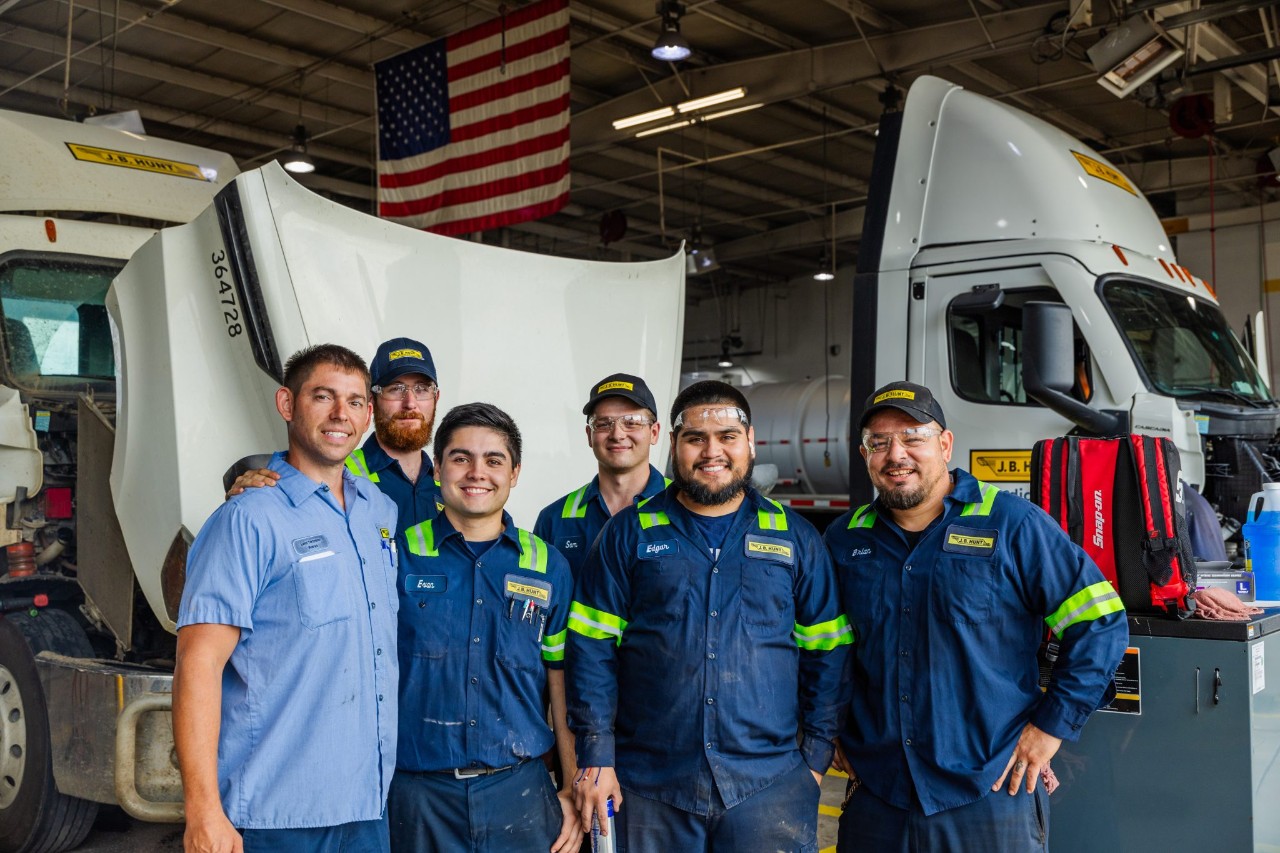 A group of J.B. Hunt maintenance technicians smile in front of a J.B. Hunt truck in a garage.