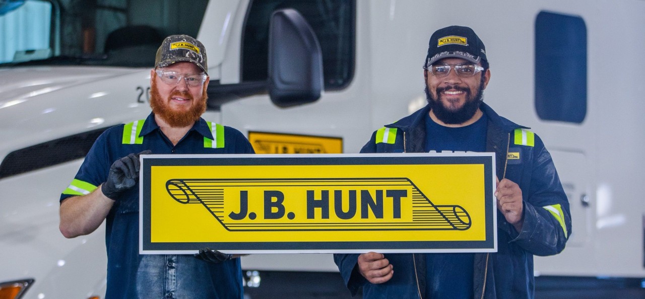 Two Maintenance employees holding up the J.B. Hunt yellow scroll cutout.