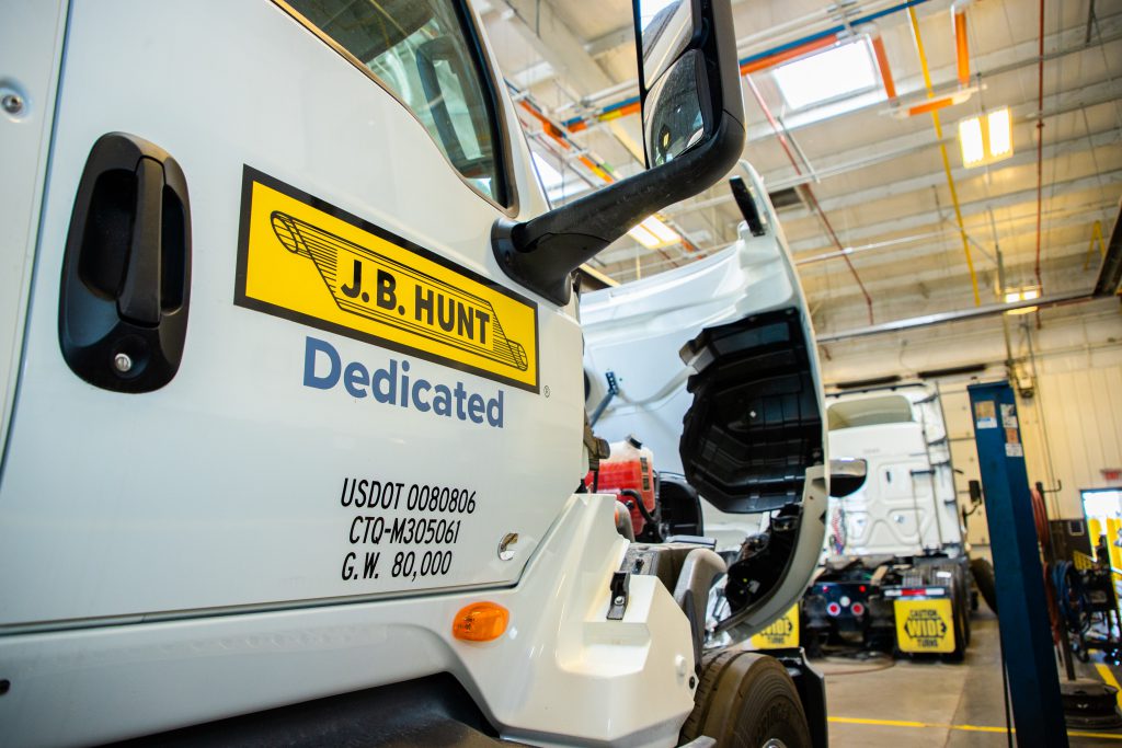 A white Dedicated trailer truck being serviced in a J.B. Hunt equipment maintenance shop.