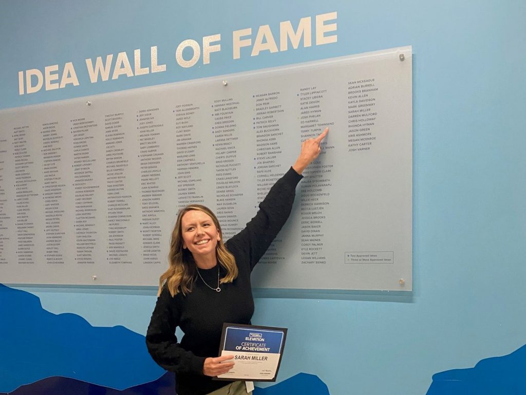 Female J.B. Hunt employee points to her name on the ELEVATION Wall of Fame.