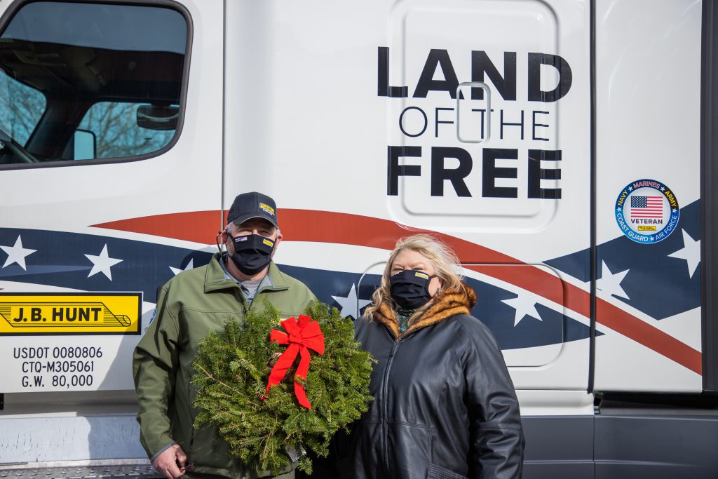 J.B. Hunt employees pose with wreath in front of a J.B. Hunt Wreaths Across America truck.