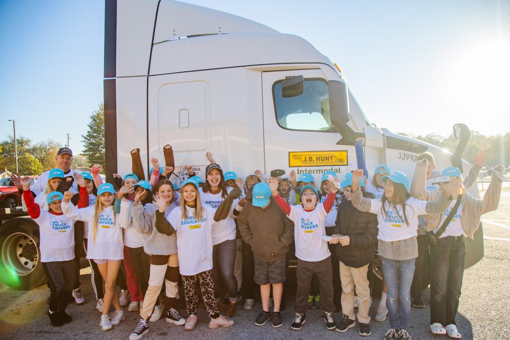 Many children in front of a J.B. Hunt semi-truck with their arms up celebrating the Adopt-a-Class program.