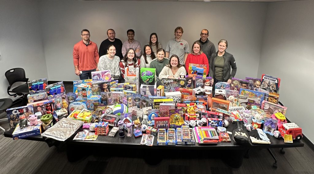 Fourteen people standing behind a table filled with toys.