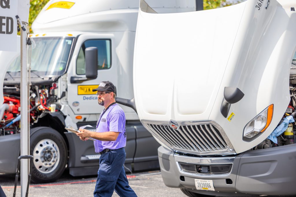 Attendee at the Zenon competition holds a clipboard next to a semi truck with an open hood