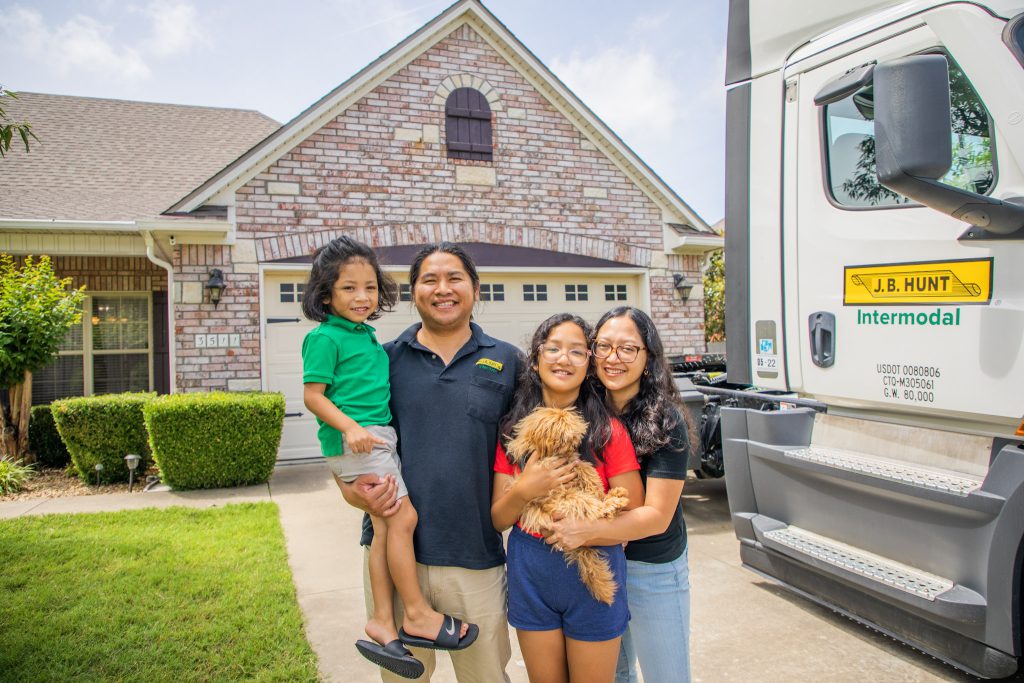 J.B. Hunt driver stands with their family in front of a house next to a J.B. Hunt intermodal truck that is parked in the driveway