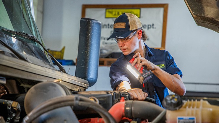 J.B. Hunt maintenance tech shining a light into a semi truck engine