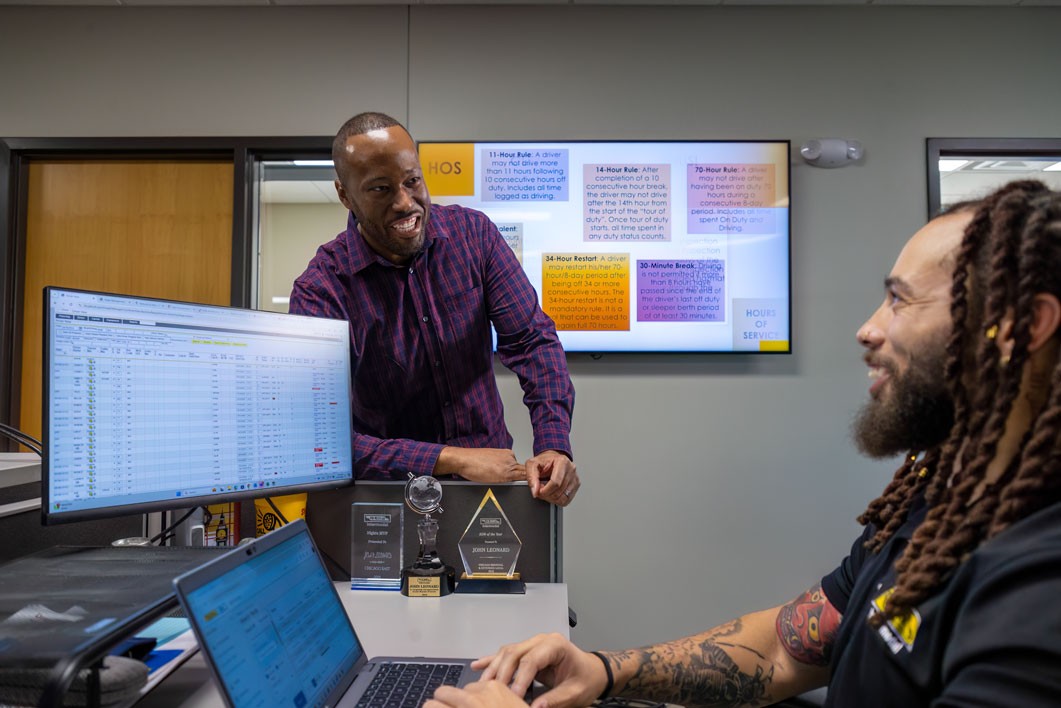 two employees talking to each other at one employee's desk
