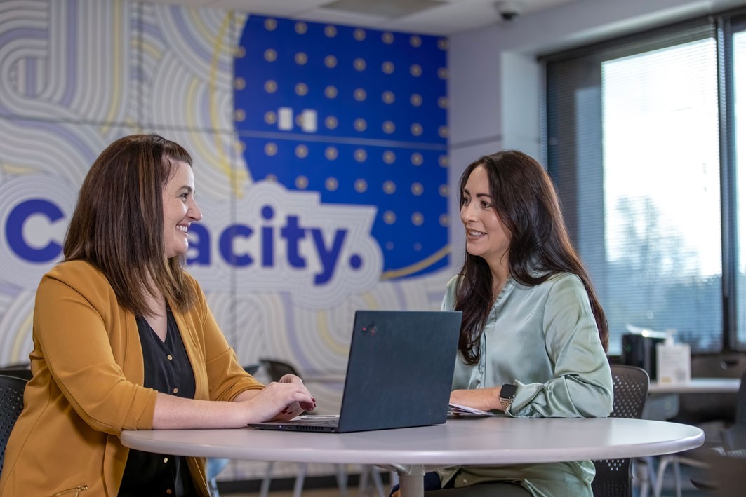 two women meeting at a small table with a laptop