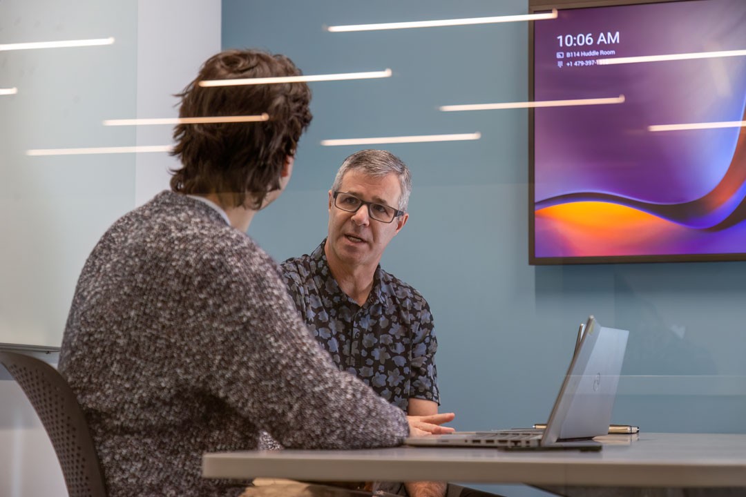 two men in a meeting room with laptop