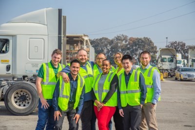 Eight J.B. Hunt employees in high visibility vests standing in a Truck yard